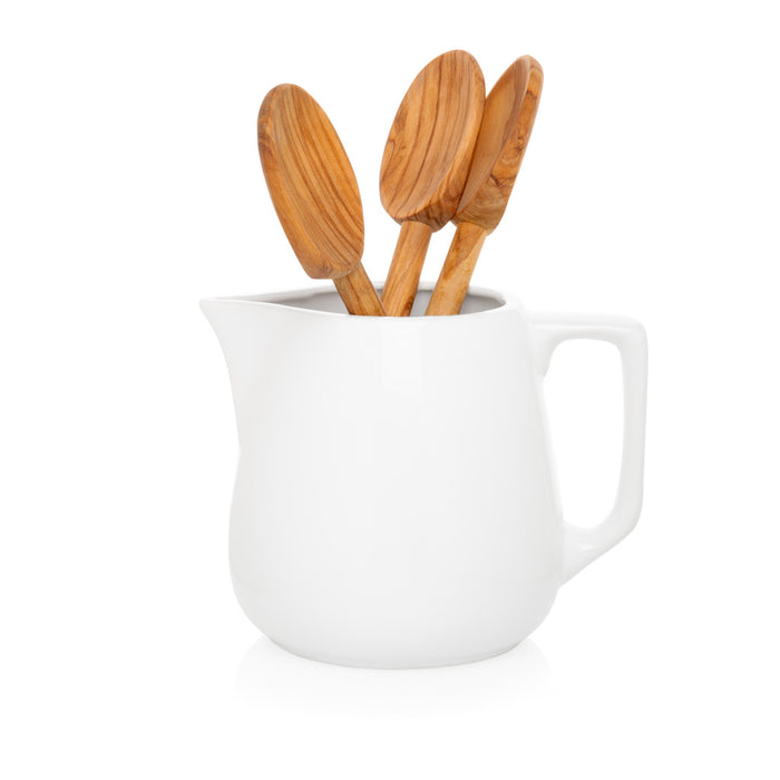 White ceramic small milk pitcher with a handle, holding three wooden spoons.