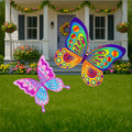 Two decorative butterfly garden signs in bright colors, a large blue and yellow butterfly and a small pink butterfly, displayed on a lawn in front of a house.