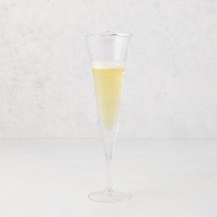 Small, clear scissor-cut glass champagne flute with a rippled rim, filled with bubbly champagne.