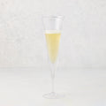Small, clear scissor-cut glass champagne flute with a rippled rim, filled with bubbly champagne.