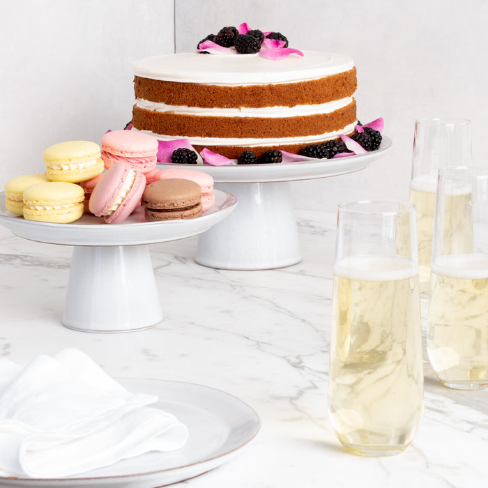 Clear stemless champagne flutes filled with sparkling wine, next to a cake and macarons.