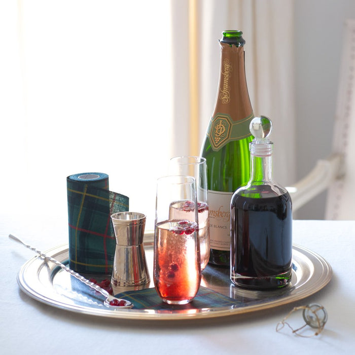 Two Hudson Grace stemless champagne flutes with cranberry drinks on a silver tray with a champagne bottle.