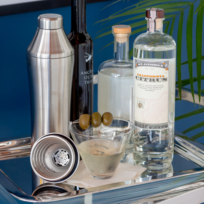 Hudson Grace Stemless Martini Glass, clear glass, with olives on a pick, on a silver tray with cocktail ingredients.