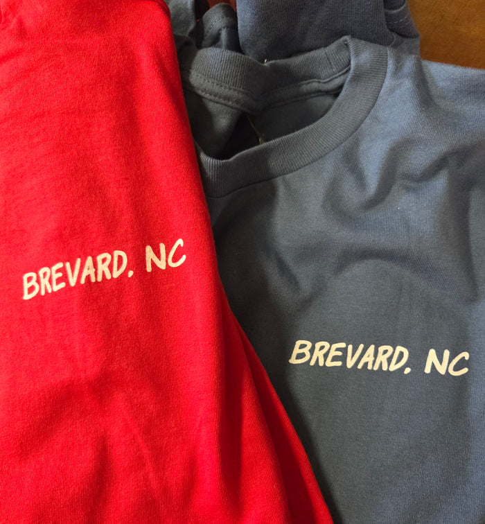 Two shirts, one red and one indigo blue, with 'Brevard, NC' printed on the front