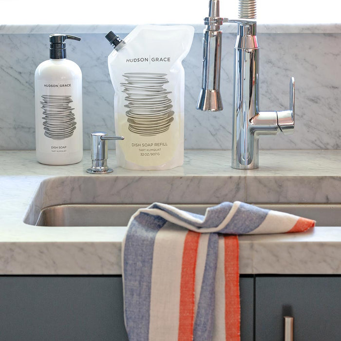 HG Tart Kumquat Dish Soap Refill Pouch and pump bottle on a marble counter with a striped towel.