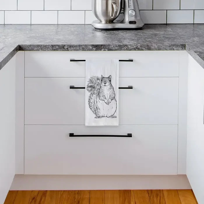 Kitchen with white cabinets, black handles, and a towel with a squirrel design hanging on one of the doors.