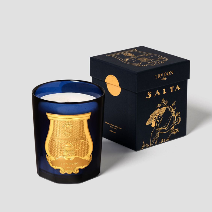 Trudon Salta Classic Scented Candle in a deep blue glass vessel with a gold emblem, next to its matching navy and gold box.