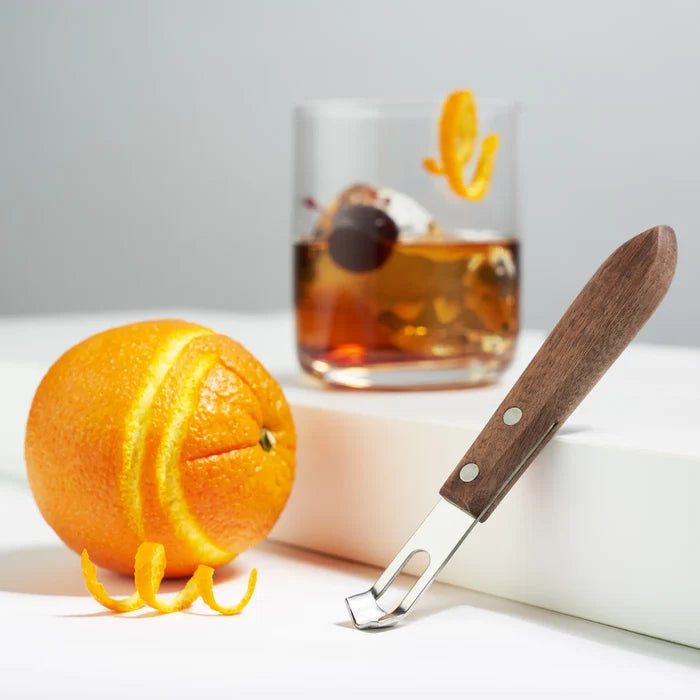 Walnut wood channel knife with stainless steel blade, next to a peeled orange and a cocktail.