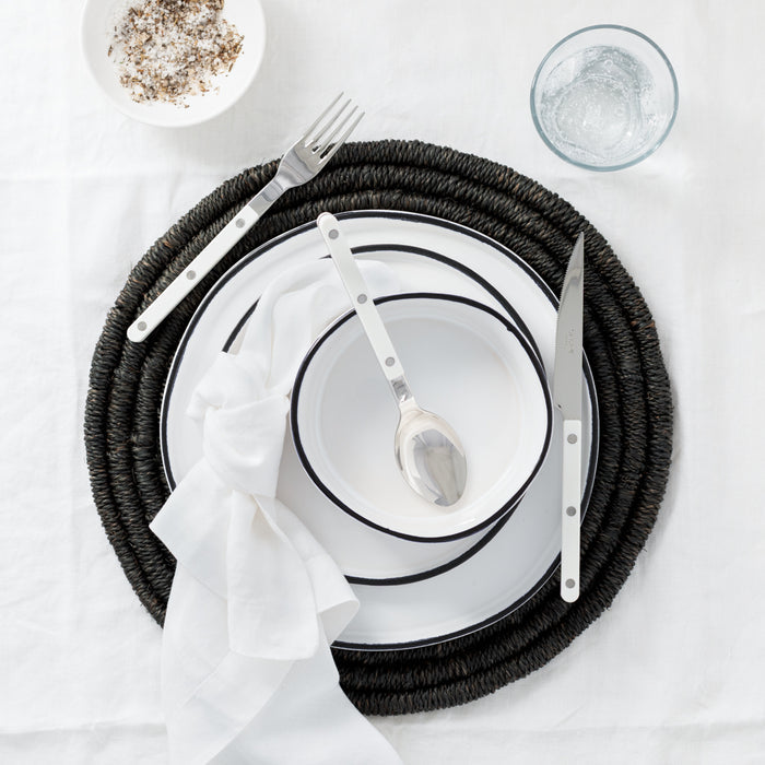 White Bistro 5-Piece Flatware Set with stainless steel and acrylic handles, on a black woven placemat.