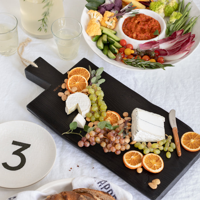 Black wooden serving board with cheeses, grapes, dried oranges, and nuts.