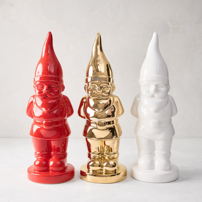 Three ceramic holiday gnomes: red, gold, and white, with pointed hats and glossy finishes.