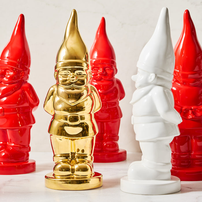 White ceramic holiday gnome with a creamy glaze, surrounded by red and one gold gnome.