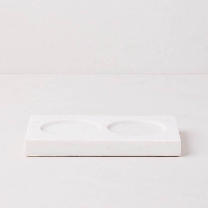 White marble rectangular tray with two circular indentations for dish soap and lotion bottles.