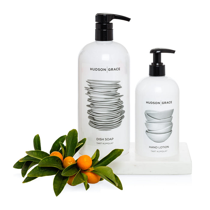 White marble dish soap and lotion tray holding two white bottles with black pumps, next to kumquat branches.