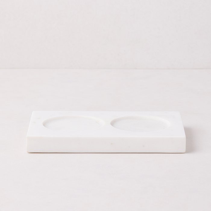 White marble rectangular tray with two circular indentations for soap and lotion bottles.
