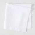 White HG Signature hand-dyed 22" square linen napkin, folded on a light surface.