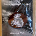 Metallic oval zipper pull with a white squirrel eating a nut on a brown background.