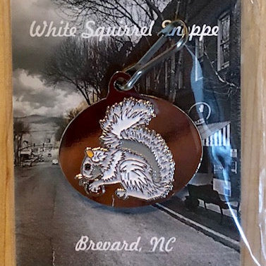Metallic oval zipper pull with a white squirrel eating a nut on a brown background.